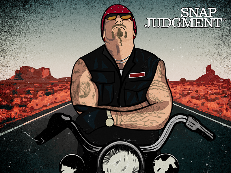 A man with tattoos has his arms crossed and is sitting on his motorcycle on the open road. He looks tough and is wearing glasses and a hat.
