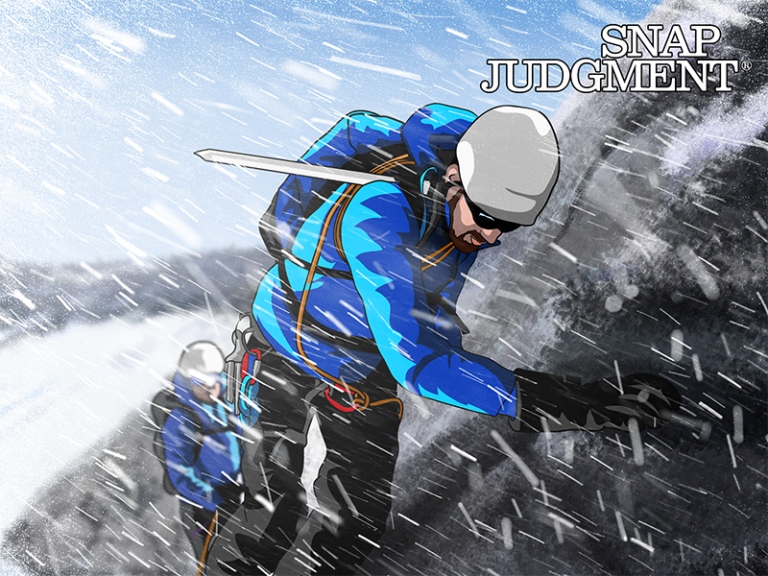 A mountain climber is on the edge of a rock, in the mountains. It is snowing.